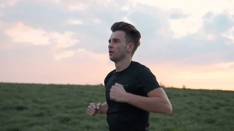 Man athlete running between meadows during colourful sunset, slow motion Stock Footage 129612031