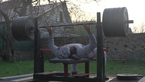 A man, an athlete, is training outdoors, doing chest press with a barbell Stock Footage 131060391