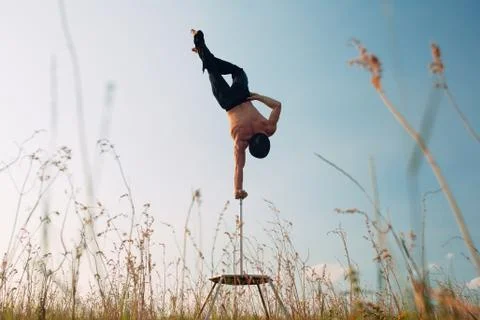 A man of athletic build performs complex gymnastic exercises in a field at Stock Photos