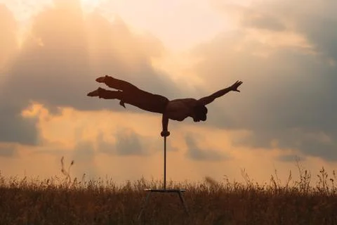 A man of athletic build performs complex gymnastic exercises in a field at Stock Photos