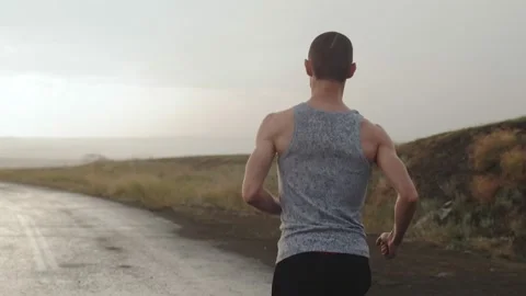 Man of athletic build runs along road in countryside during the rain, flash of Stock Footage 159646002
