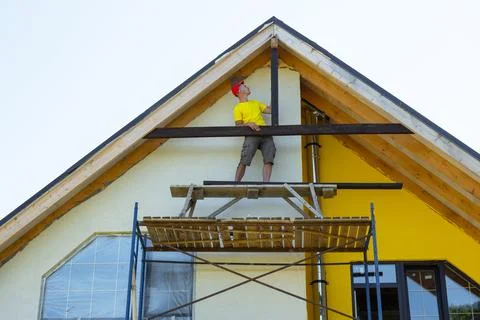Man attaches lower decorative elements to gable, uses ladder and scaffold, .. Foto stock