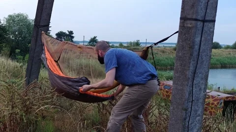 Man attaching underquilt thermal insulation to camping hammock Stock Footage 339591807