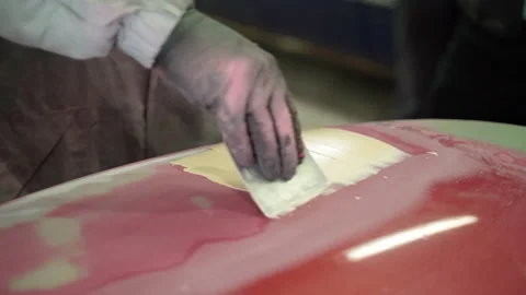 Man auto mechanic with the help of a spatula spatula applies a yellow putty Stock Footage 153488553