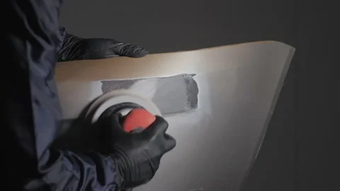 A man auto mechanic uses a grinder to grind a putty on a damaged car body part.  Stock Footage 202168001