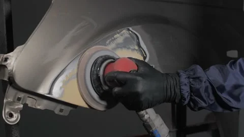 A man auto mechanic uses a grinder to grind a putty on a damaged car body part.  Video stock 202169657