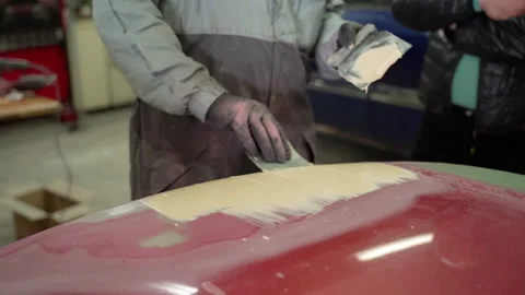 Man auto mechanic uses a spatula to put putty on the damaged part of the car Stock Footage 153488949