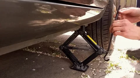 Man auto mechanic using screw jack to change tire in car. Car repair Stock Footage 246769851
