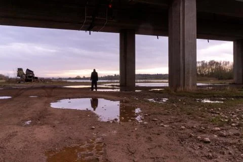 A man back to camera reflected in a puddle. Standing underneath a bridge Stock Photos
