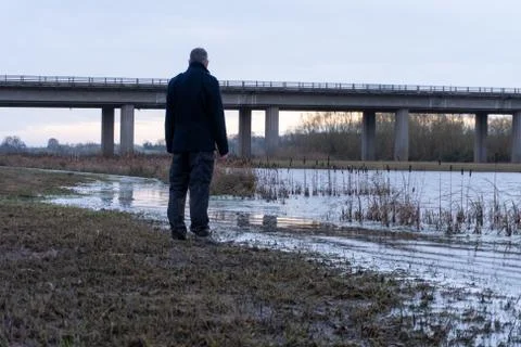 A man back to camera, standing by a lake in the countryside in winter. Stock Photos