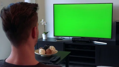 A man, the back of the head to the camera, watches a TV with a green screen in a Stock-Footage 71173348
