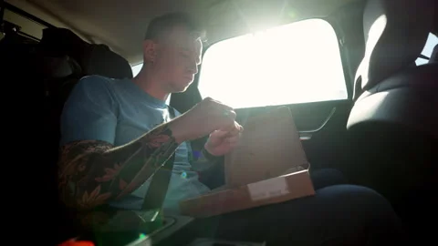 Man in the back seat of a car on a trip eating pizza. The guy enjoys a snack on Stock Footage 280511755