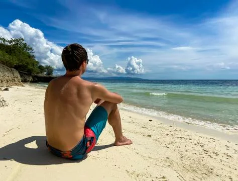 Man from the back sits on white sandy beach and looks at sea.Guy is relaxing Stock Photos