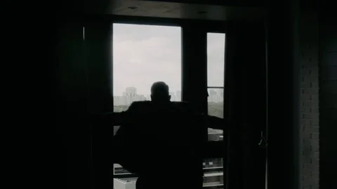 The man in the backlight puts his jacket on the window with his back to the came Stock Footage 119954357