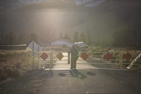 A man backlit with sun flare navigating a gate on a walking path on a cold mo Foto stock