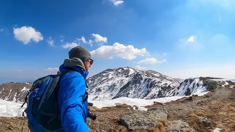 Man with backpack and hat taking selfies and looking at snow capped mountai.. Stock Photos