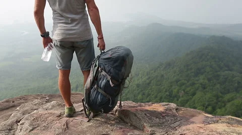 A man with backpack and  water standing on the rock  with a valley at the bottom Stock Footage 49455861