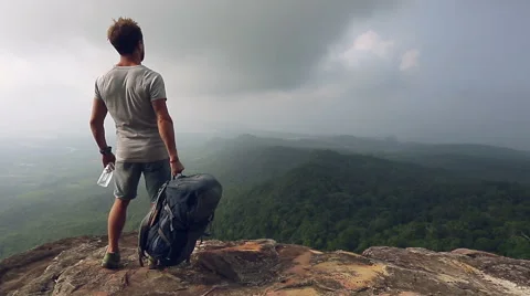 A man with backpack and water standing on the rock  with a valley at the bottom Stock Footage 49455888