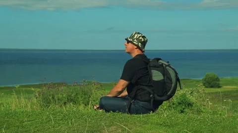 A man with a backpack behind his back sits on the edge of the mountain and Stock Footage 97351026