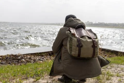 Man with a backpack behind his back squats by the water 스톡 사진