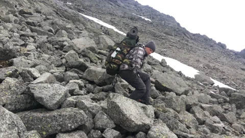A man with a backpack carefully descends sharp stones on a steep descent Stock Footage 207686469