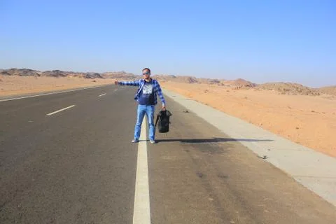A man with a backpack catches hitchhiking on a desert road Stock Photos
