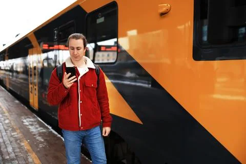 Man with backpack checking phone on railway platform next to modern orange .. Stock Photos
