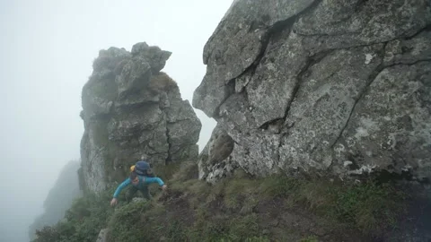 A man with a backpack climbs rocky mountains into the fog. A tourist in the rain Stock Footage 214332350