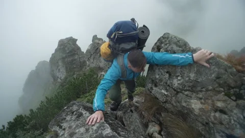 A man with a backpack climbs rocky mountains into the fog. A tourist in the rain Stock Footage 229782593