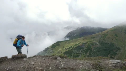 A man with a backpack climbs to the top of the mountain and celebrates Stock Footage 218442257