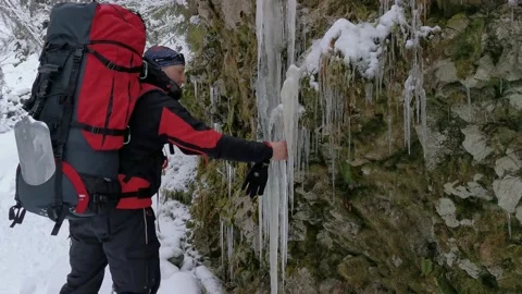 Man with a backpack comes up and bounces off a large icicle. Stock Footage 219955549