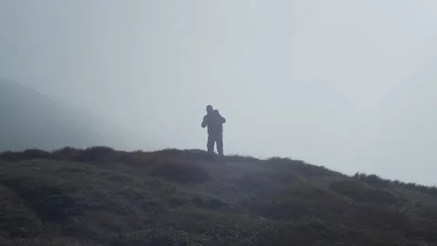A man with a backpack comes out of the fog in the mountains. Silhouette of a man Stock Footage 236557824