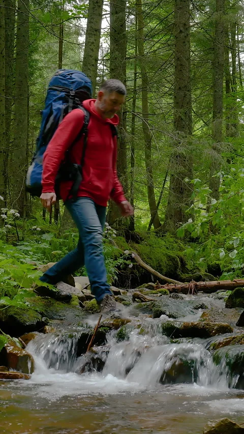A man with a backpack crosses a mountain stream in the forest Stock Footage 346119407