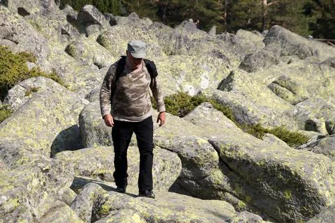 A man with a backpack descends the mountain over large boulders Stock Photos