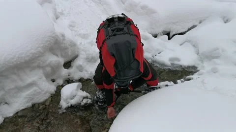 Man with a backpack drinking water from a stream on a winter hike. Video stock 219949042