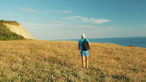 The man with the backpack goes along the slope of the mountain covered with Video stock 220681846