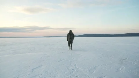 The man with the backpack goes far along the frozen lake covered with snow Видео 239141669