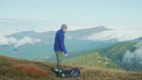 A man with a backpack on a hike, stops to look at the mountains at the landscape Stock Footage 238757250