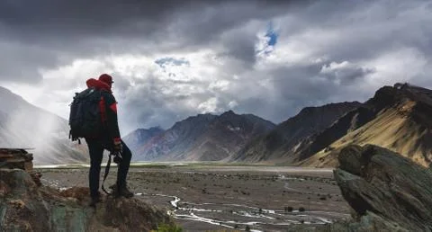 A man with backpack holding camera standing on cliff with mountains view Stock Photos