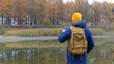 Man with backpack holds smartphone while walking in autumn. hiker with phon.. Stock Photos