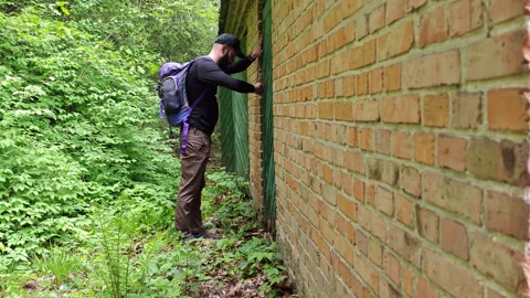 Man with backpack inspecting green wooden door on old brick house Stock Footage 336970853