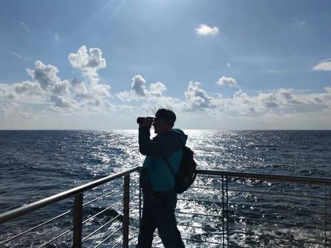 A man with a backpack looks through binoculars at the sea horizon Stock Photos