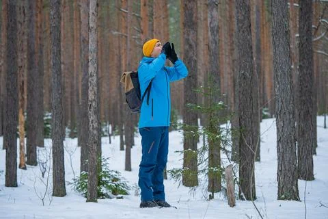 Man with a backpack lost in a winter forest, wearing warm clothing and making a Stock Photos