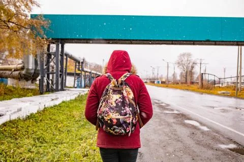 A man with a backpack in a red jacket is walking along the road in autumn Foto stock