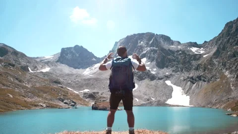 Man with a backpack resting on a mountain lake Stock Footage 138445353