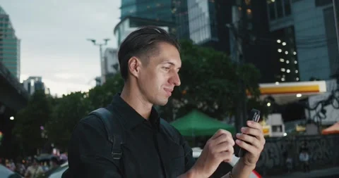 Man with backpack scrolling smartphone among glowing lights night metropolis Stock Footage 252210555