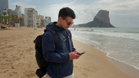 Man with backpack sending message on beach travel lifestyle concept 動画素材 333690465