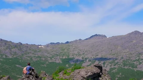 A man with a backpack sits on a rock and looks at a beautiful panorama Stock Footage 135188997