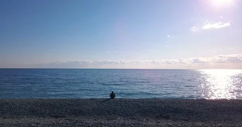A man with a backpack sits on the shore and looks into the distance. Tourist Stock Footage 128735790