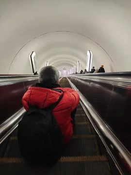 A man with a backpack sits on the steps of an escalator and descends Stock Photos